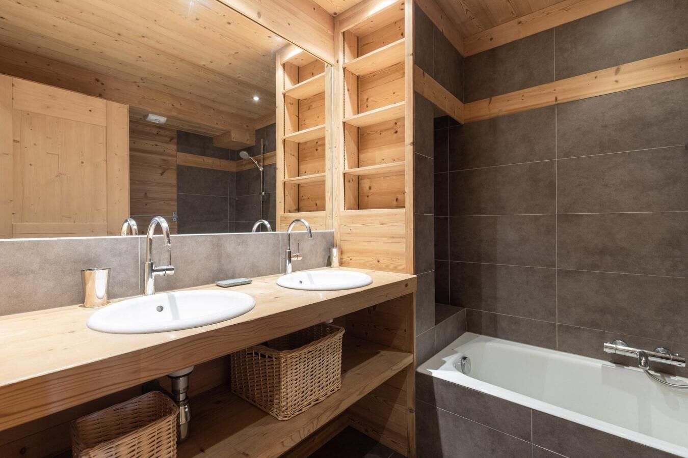 Une salle de bain moderne avec des étagères en bois, deux lavabos, un grand miroir et une baignoire.