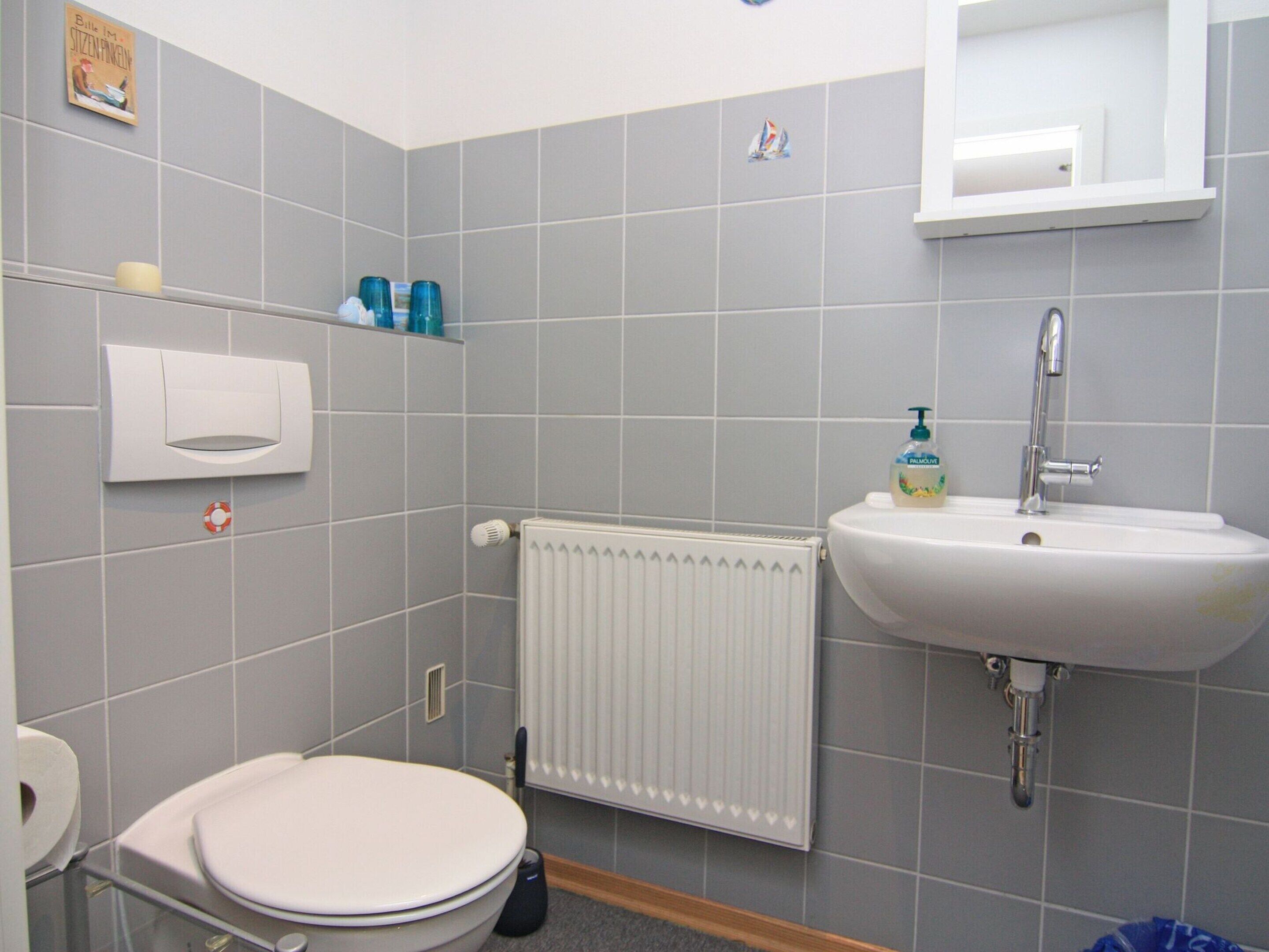 A bathroom with a toilet, a sink, a radiator, and a shelf with toiletries.
