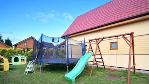 Ein Garten mit Trampolin, Rutsche, Schaukel und einem kleinen Spielhaus.