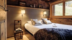A cozy room with a wooden ceiling, a bed with white bedding, a small bedside table, and a window with a view of greenery.