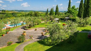 A landscaped garden with a swimming pool, stone pathways, and tall cypress trees. - Apartment in Montaione With Fireplace (Montaione)