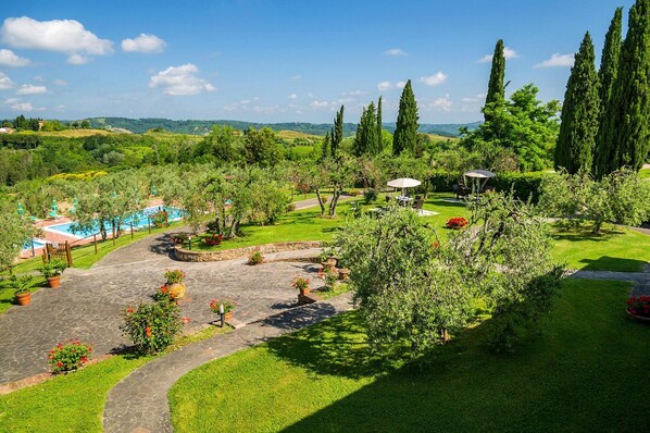 Un jardin aménagé avec une piscine, des allées pavées et de grands cyprès.