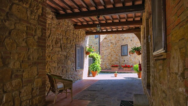 A stone-walled courtyard with a wooden bench, potted plants, and a fire extinguisher. - Apartment in Montaione With Fireplace (Montaione)
