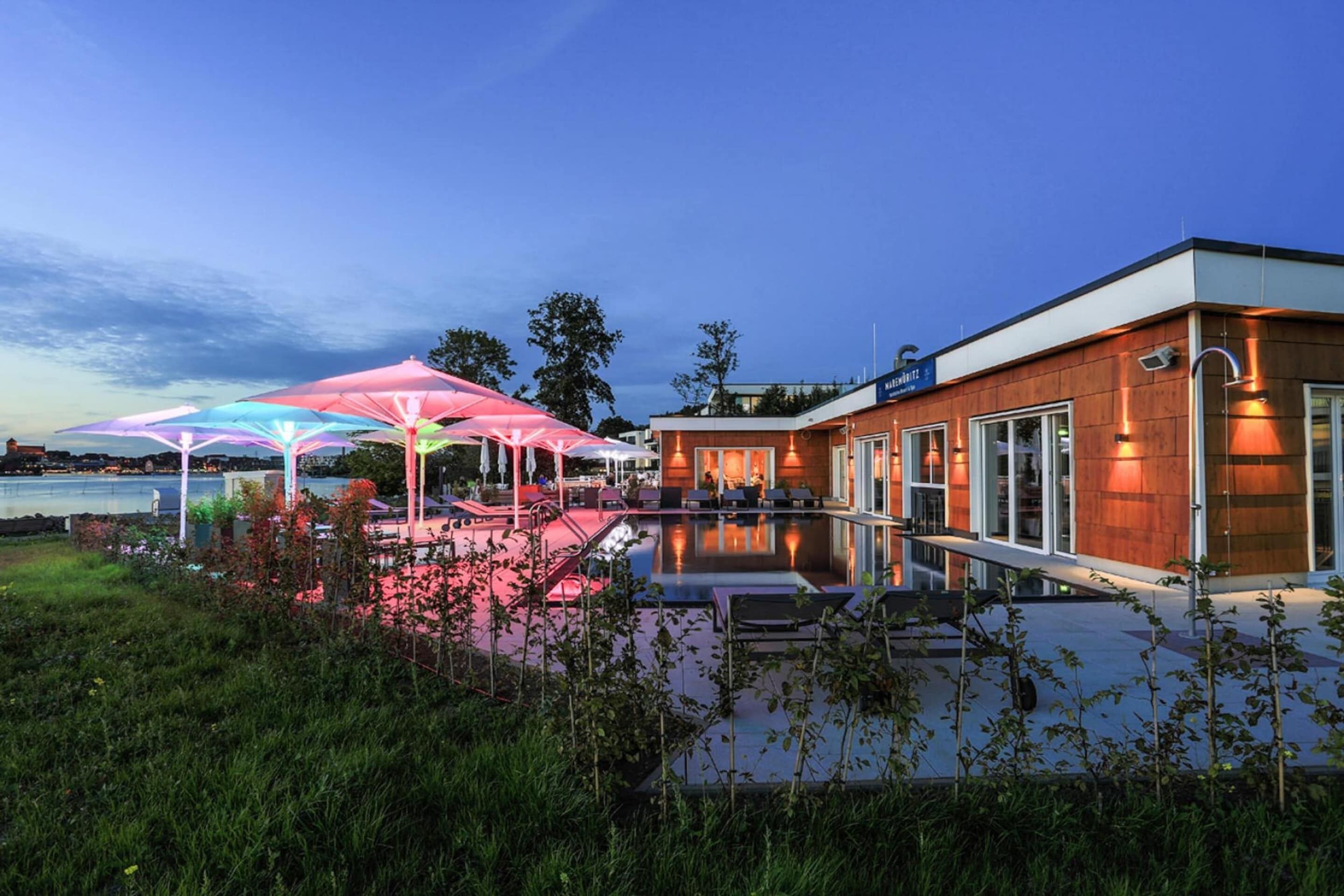 Un edificio moderno con piscina y zona de estar exterior con sombrillas.
