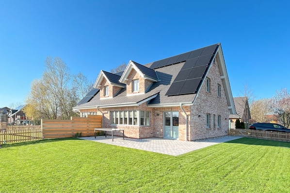 A two-story house with a sloped roof, solar panels, and a well-maintained lawn.