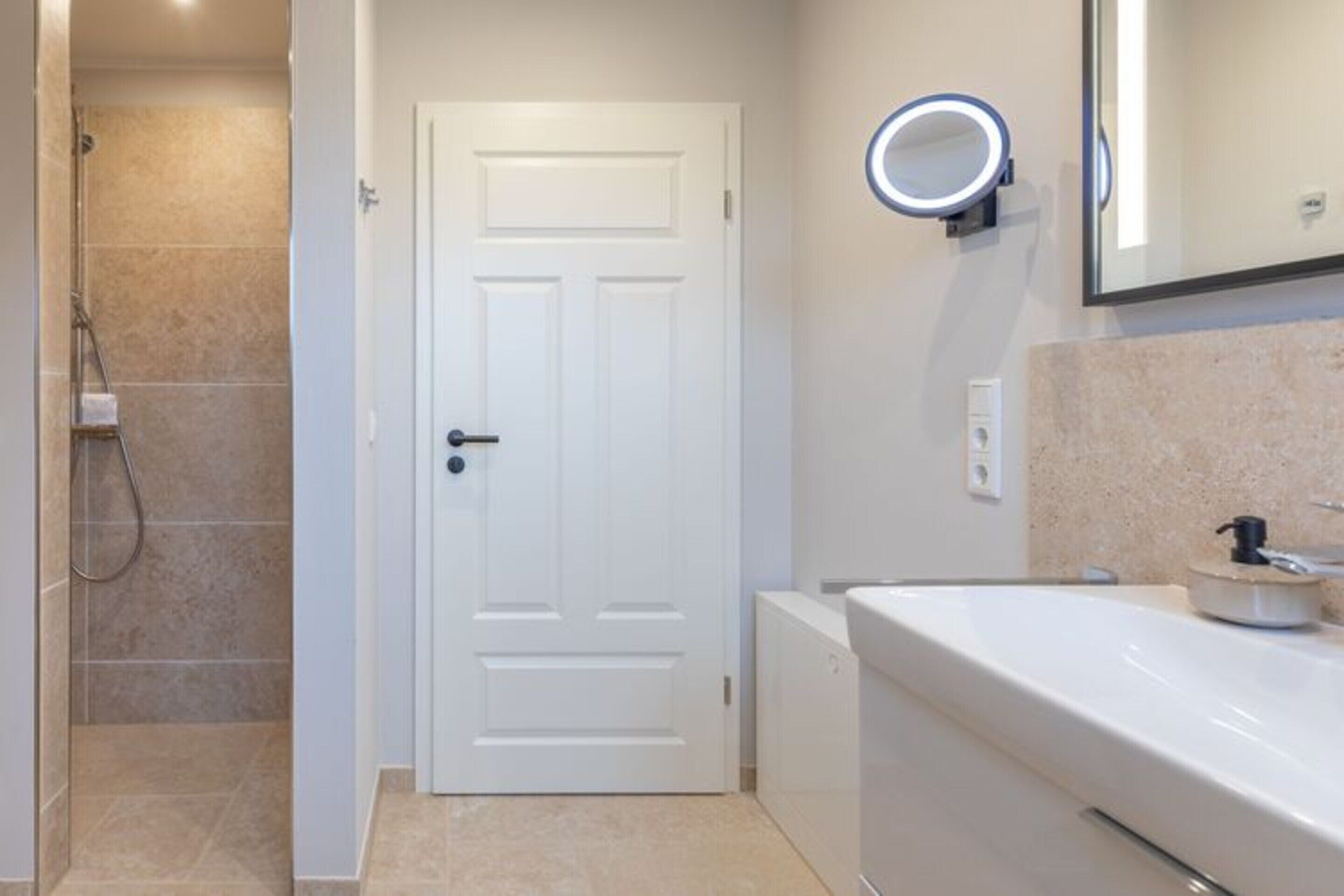 A bathroom with a white door, a shower, a sink with a mirror, and a light fixture above the mirror.