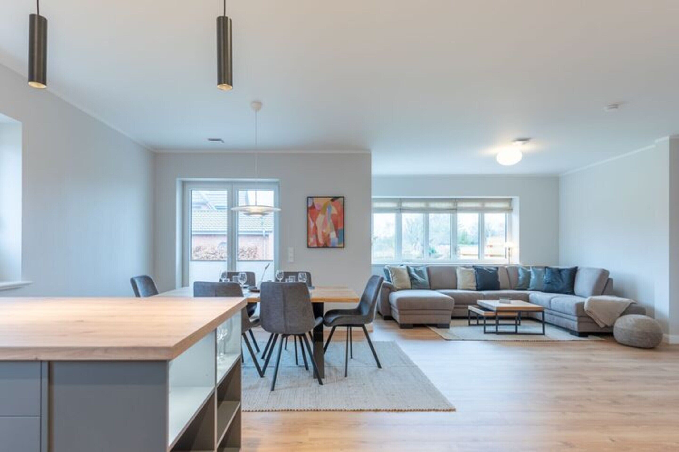 Een ruime woonkamer met een houten eettafel, grijze stoelen, een grijze bank en een bijzettafeltje.