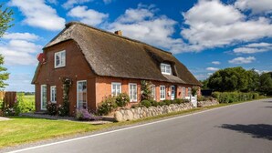 Ett traditionellt hus byggt av tegel med ett halmtak, en stenmur och en välskött trädgård.