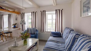 Ett vardagsrum med en randig soffa, ett soffbord med en vas, en stol och ett fönster med gardiner.