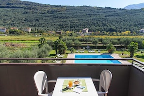 A balcony with a table, two chairs, and a view of a swimming pool, vineyards, and a hillside. - Residence Moinca at Riva del Garda (Riva del Garda)