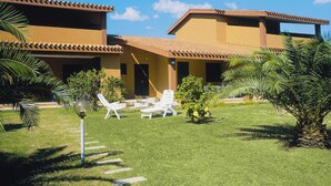 Un hotel con un cortile che presenta un prato, palme e poltrone relax.