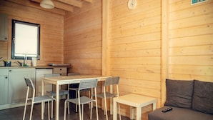 Een gezellige, compacte leefruimte met houten details, een eethoek met tafel en stoelen, een bank en een kitchenette.