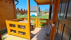 Een houten blokhut met een overdekte veranda, buitenmeubels en uitzicht op andere blokhutten.