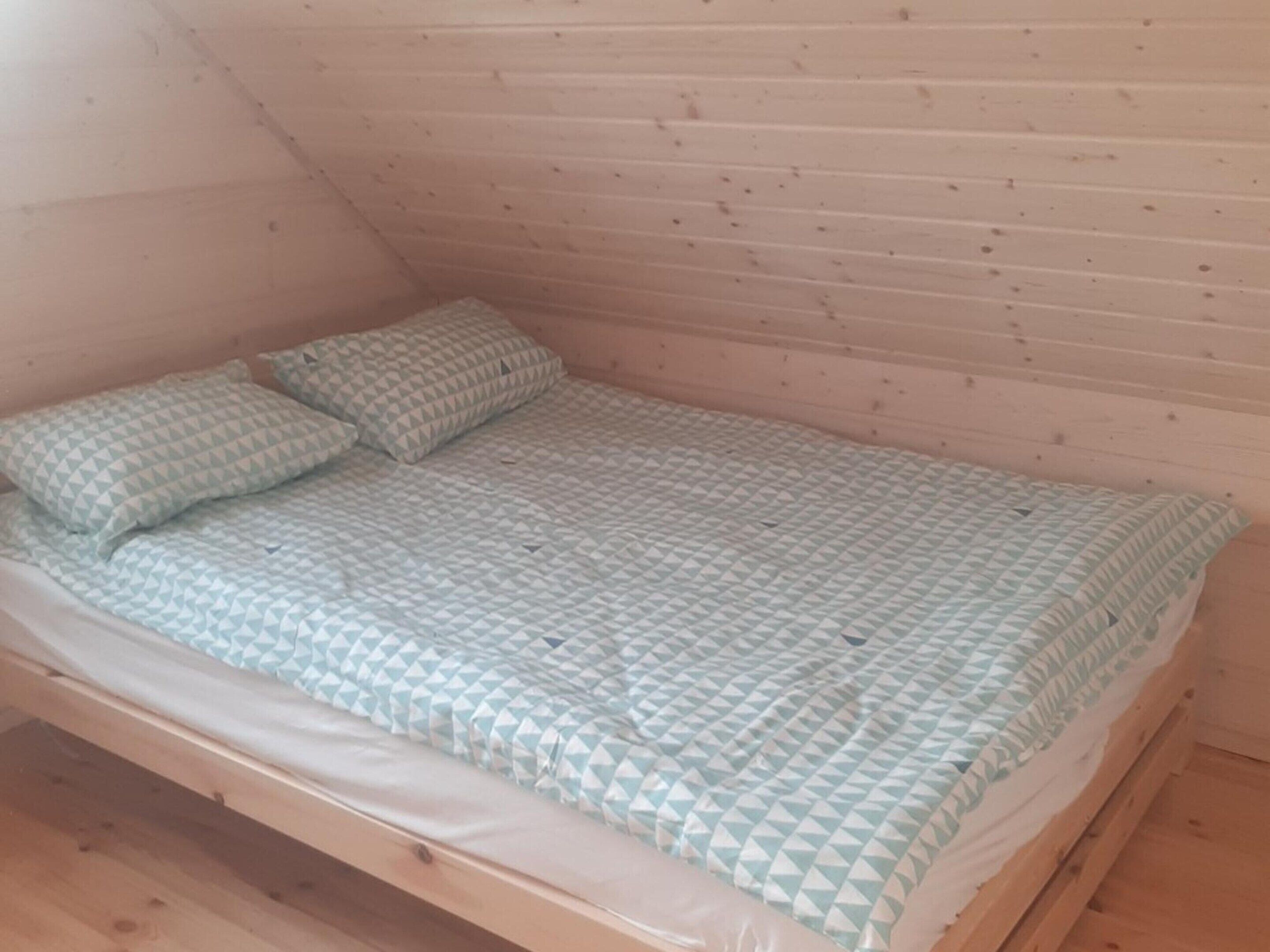 Un lit simple avec une couvre-lit à motifs et des oreillers, dans une pièce aux murs en bois et au plafond en pente.