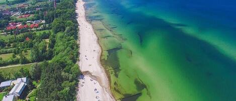 An aerial view of a coastal area with a beach, buildings, and greenery.