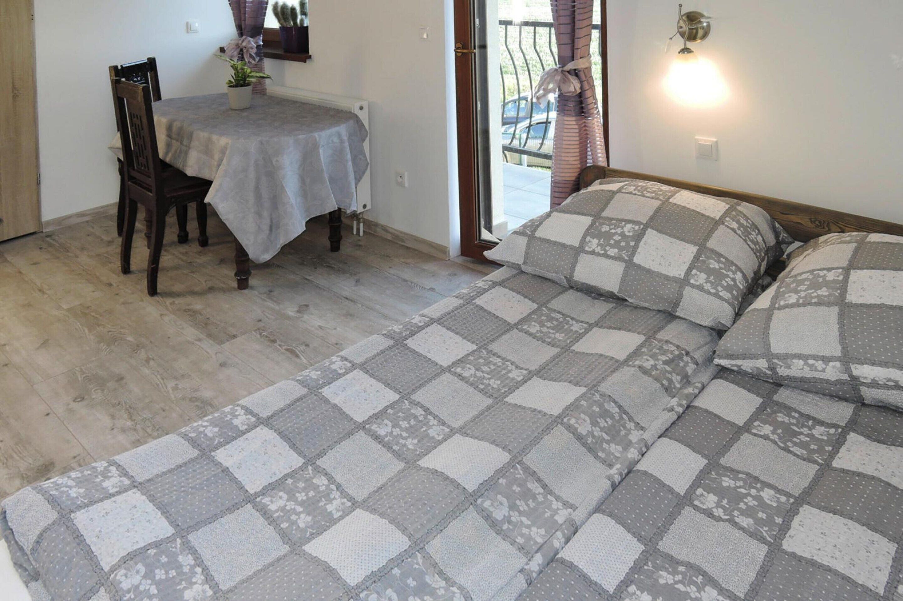 A bedroom with a checkered bedspread, a dining table with chairs, and a potted plant.