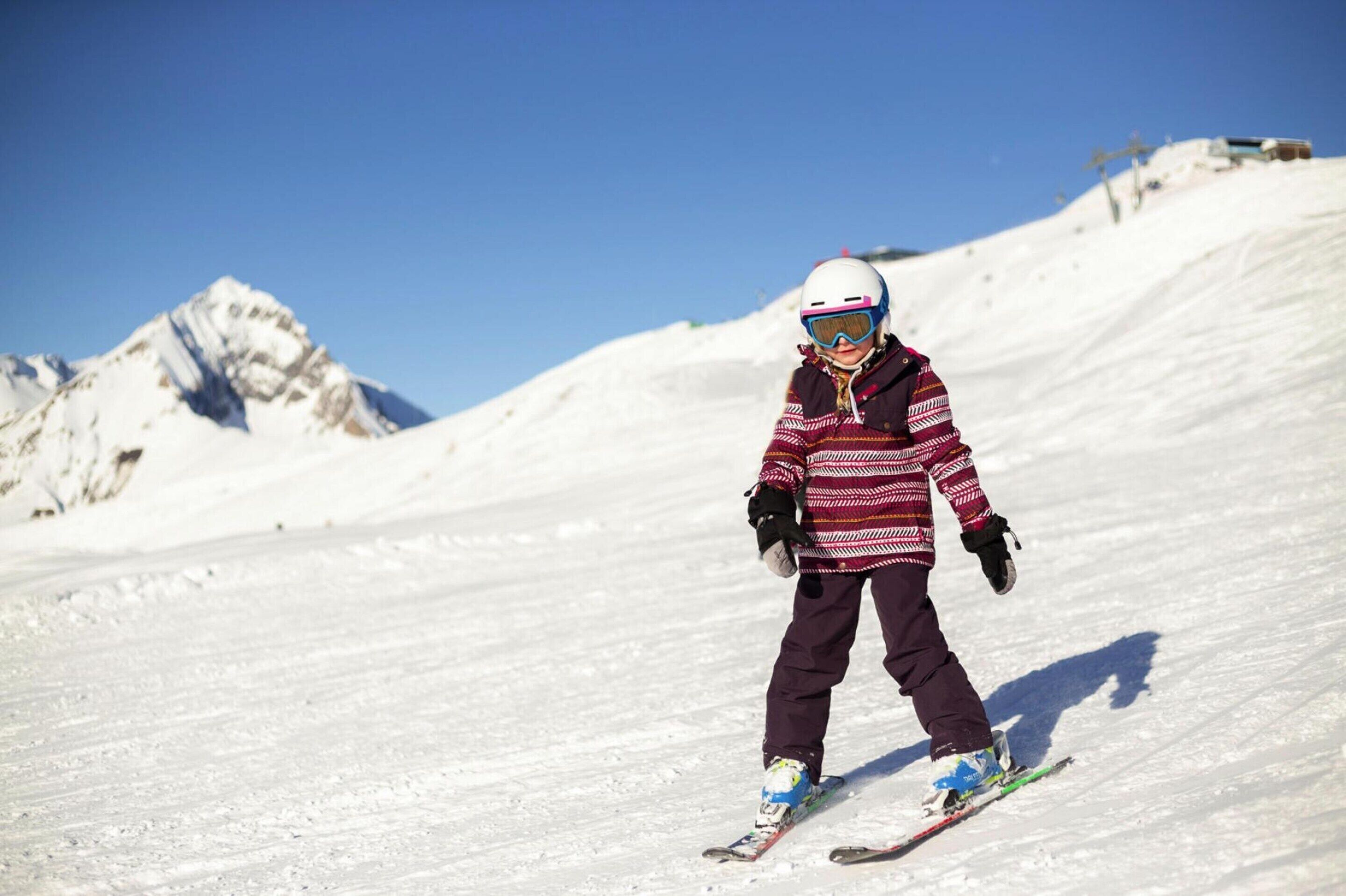 A person skiing on a snowy slope with a clear sky and mountains in the background.