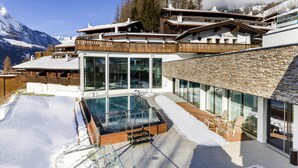 Une station de ski moderne dotée d’une piscine couverte, d’une terrasse en bois et offrant une vue sur les montagnes.