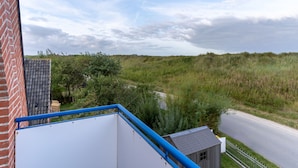 A view from a balcony overlooking a grassy field with a road and a small building. - Wohnung in St. Peter Ording (St. Peter-Ording)