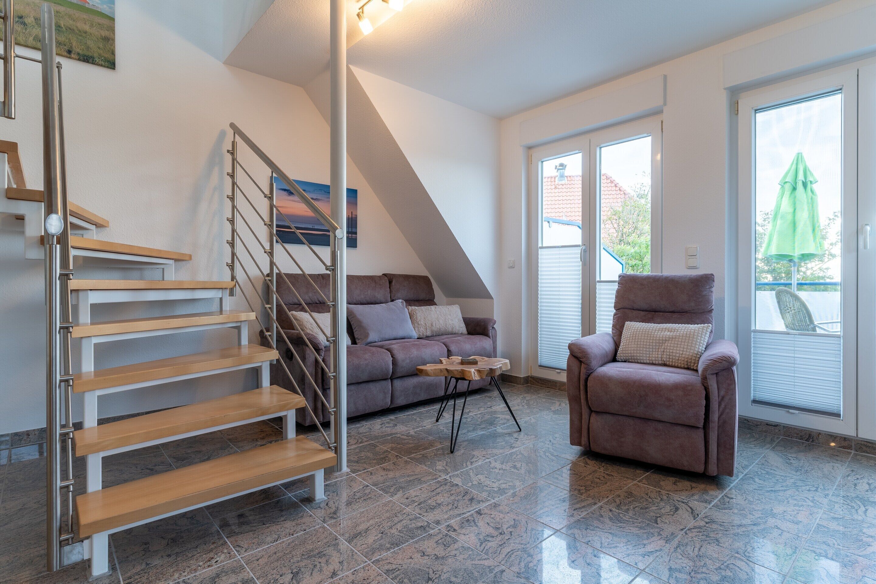 Una sala de estar moderna con una escalera, un sofá, un sillón reclinable y una mesa de comedor.
