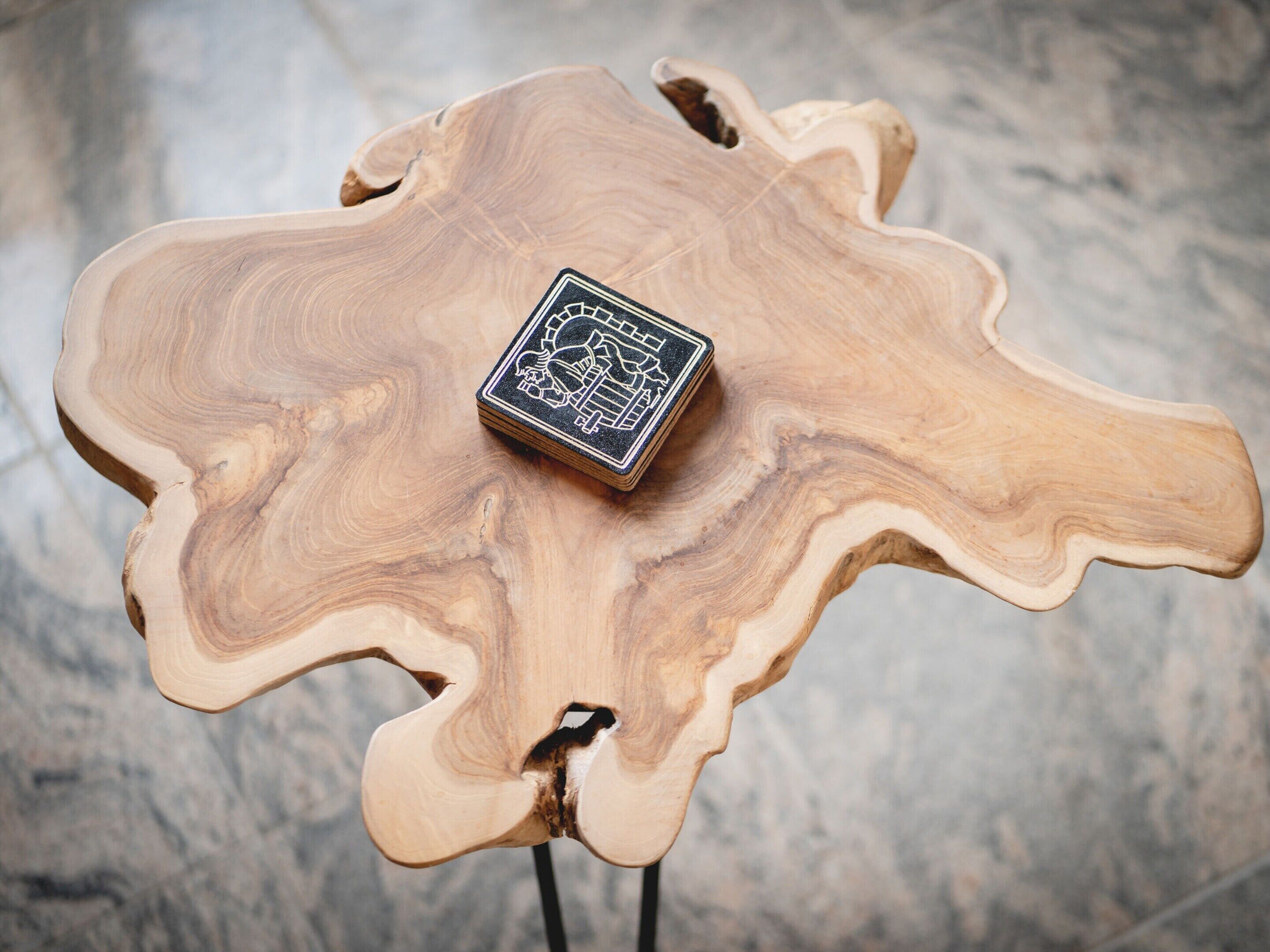 A wooden table with a unique wavy edge design and a black square object on top.