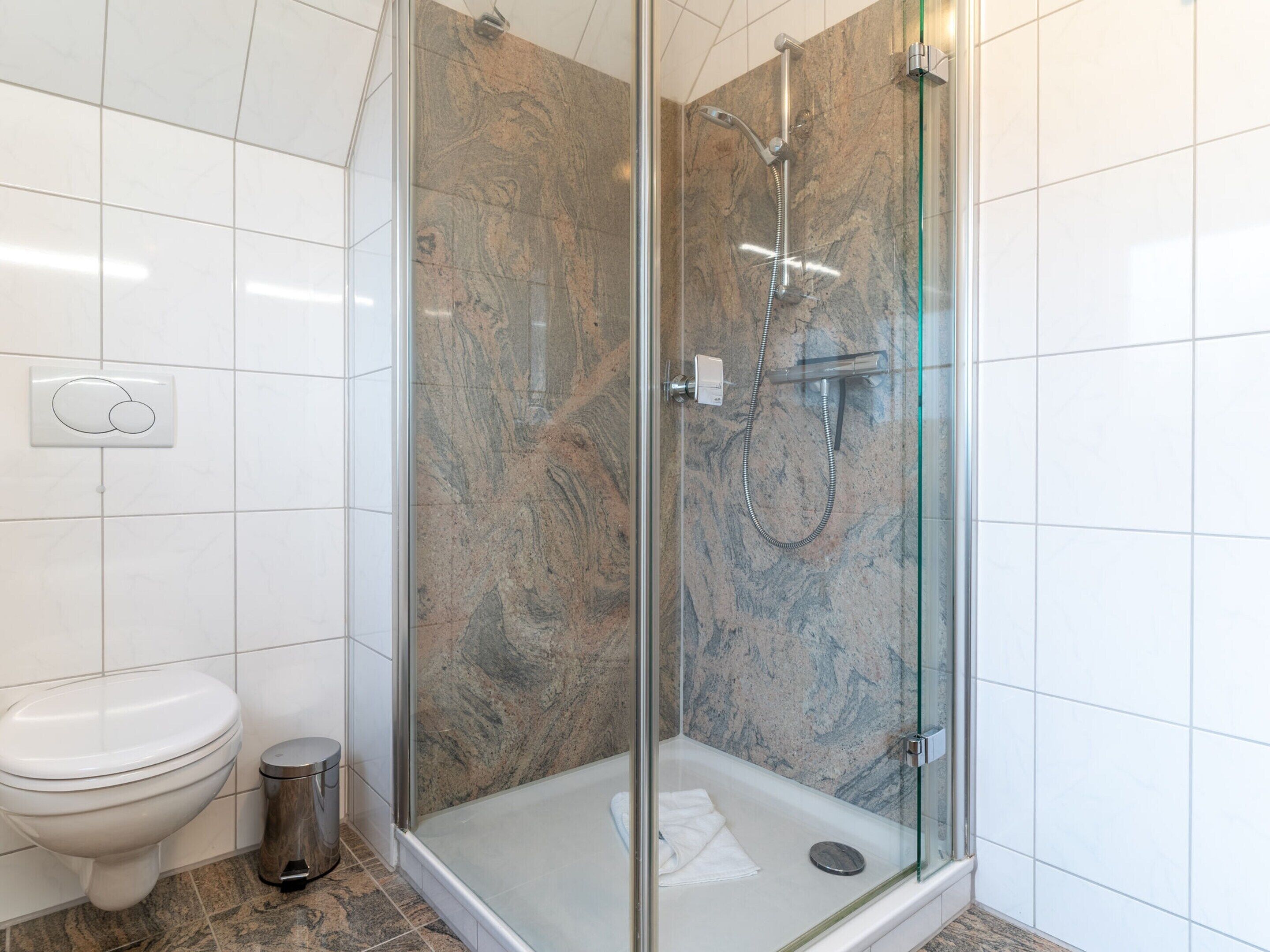 Un baño moderno con cabina de ducha de vidrio, inodoro y cubo de basura.