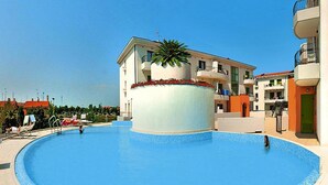 A swimming pool with a central fountain, surrounded by a tiled deck. - Holiday Flat Galeria Gran Mado in Caorle (Caorle)