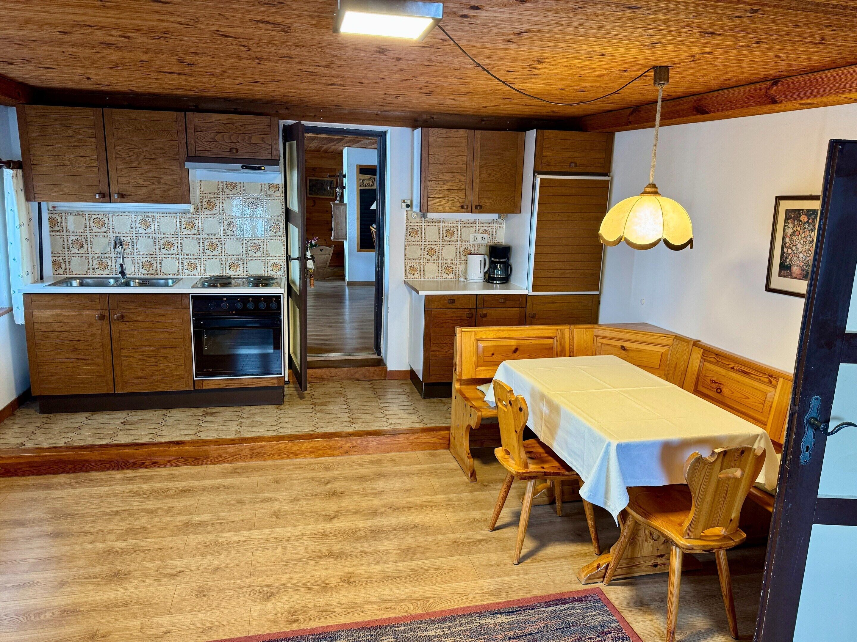 Ett mysigt kök med träskåp, ett matbord med stolar och en hängande lampa.