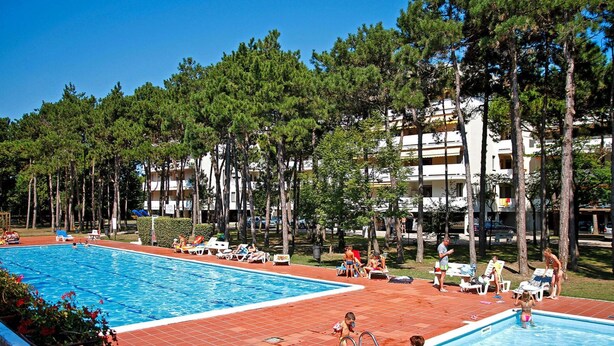 Area piscina con due vasche, circondata da alberi e un edificio con numerosi balconi.