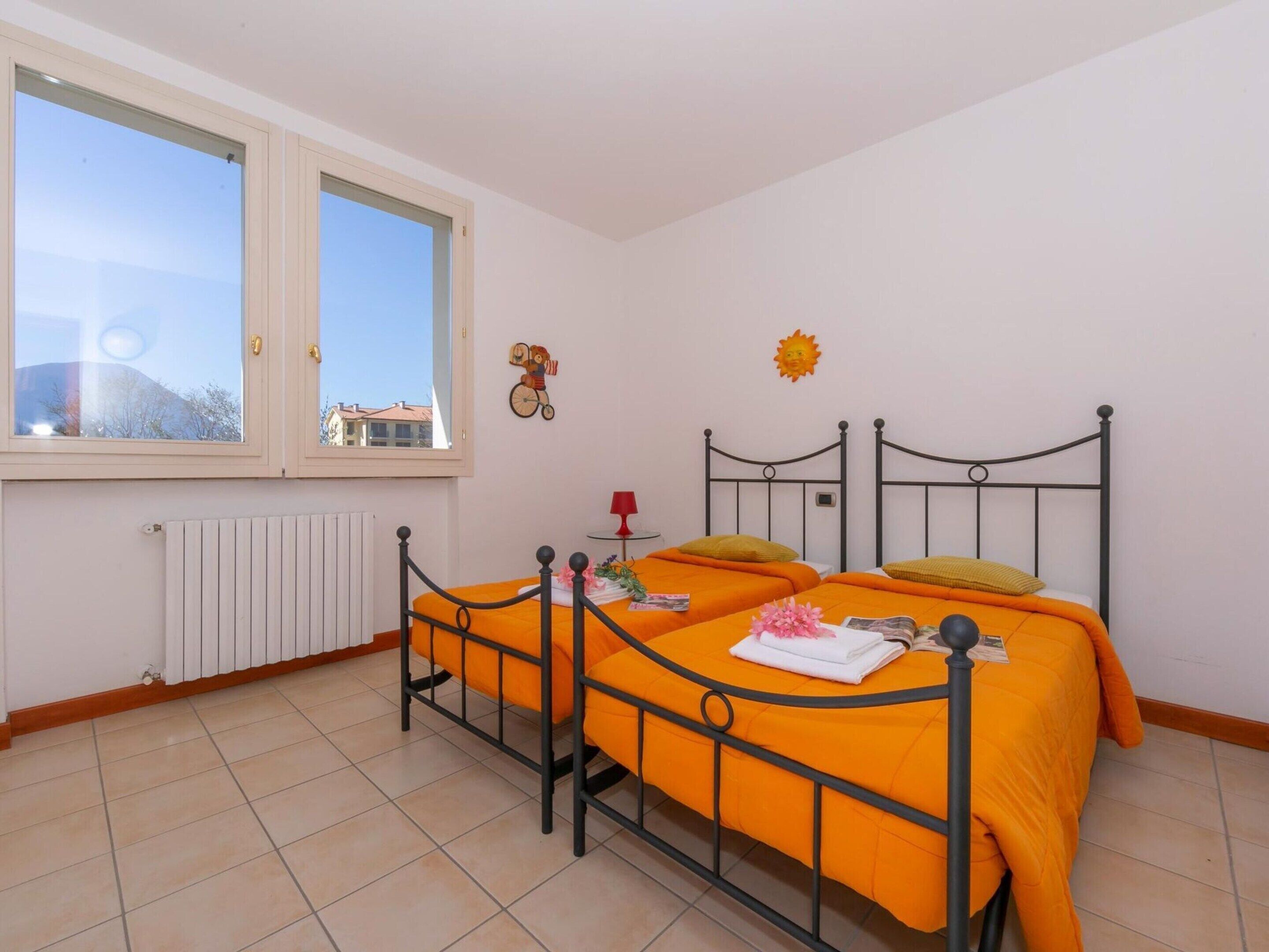 A bedroom with two beds, a window, a radiator, and a wall decoration.