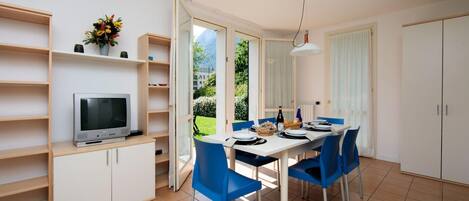 Una cocina moderna con comedor, estanterías abiertas, televisor y vistas al exterior.