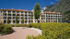 Un hotel de varios pisos con balcones, un patio empedrado y montañas al fondo.