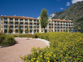 Un hotel de varios pisos con balcones, un patio empedrado y montañas al fondo.