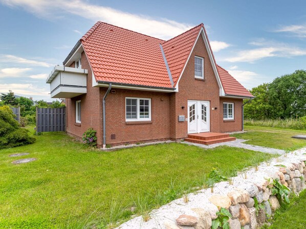 A two-story house with a red-tiled roof, a brick exterior, and a stone wall in the front yard. - Wohnung in St.peter Ording (St. Peter-Ording)