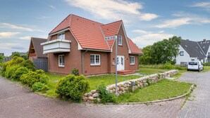 A two-story brick house with a red-tiled roof, a front porch, and a stone wall. - Wohnung in St.peter Ording (St. Peter-Ording)
