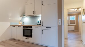 A modern kitchen with white cabinets, a built-in oven, and a countertop with a coffee maker. - Wohnung in St.peter Ording (St. Peter-Ording)