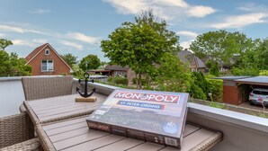 A Monopoly board game on a wicker table on a balcony with a view of houses and trees. - Wohnung in St.peter Ording (St. Peter-Ording)