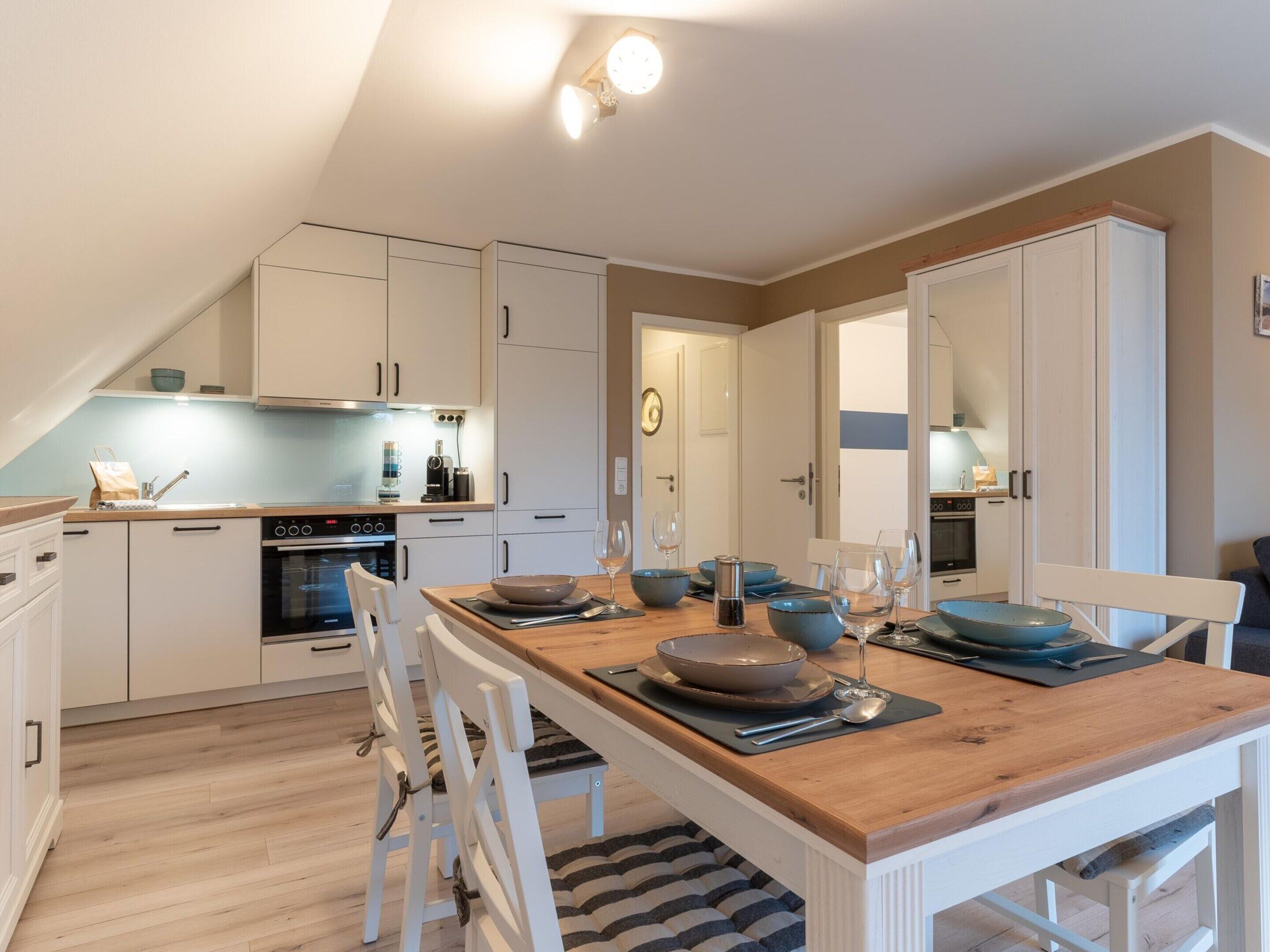 A modern kitchen with white cabinets, a wooden dining table set for four, and a built-in oven.
