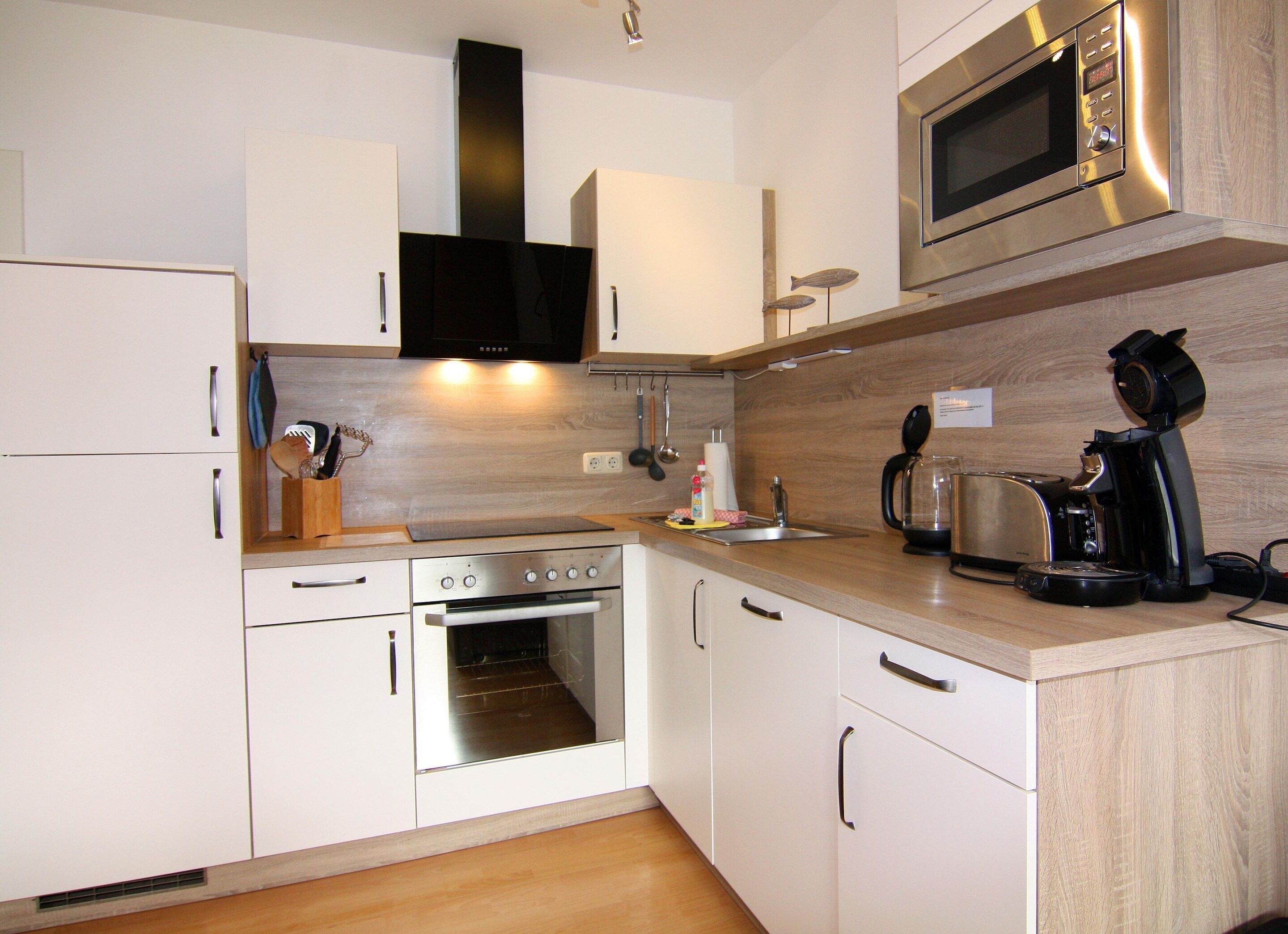 Een moderne keuken met witte kastjes, roestvrijstalen apparatuur en houten aanrechtbladen.