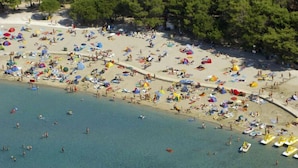 Eine Luftaufnahme eines überfüllten Strandes mit vielen Sonnenschirmen und Zelten, was auf ein beliebtes Urlaubsziel hindeutet.