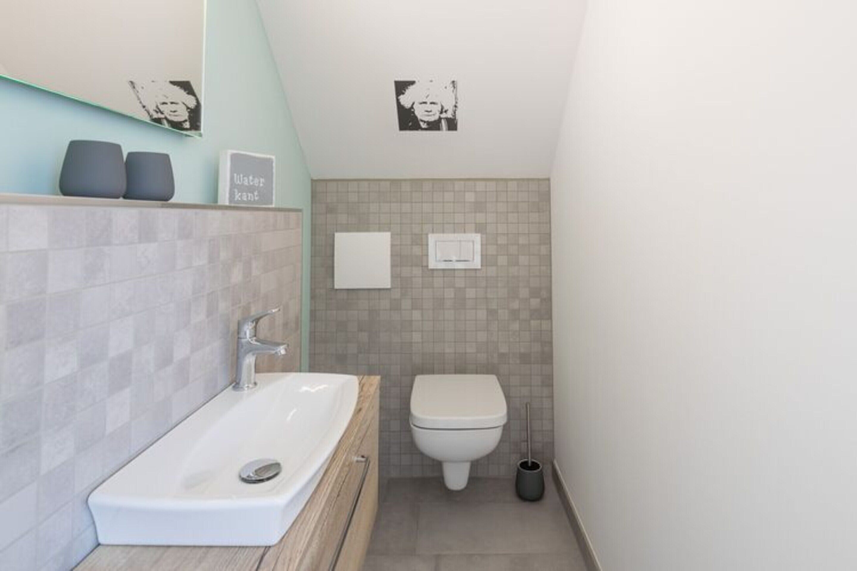 A modern bathroom with a white sink, a toilet, and a small trash bin.