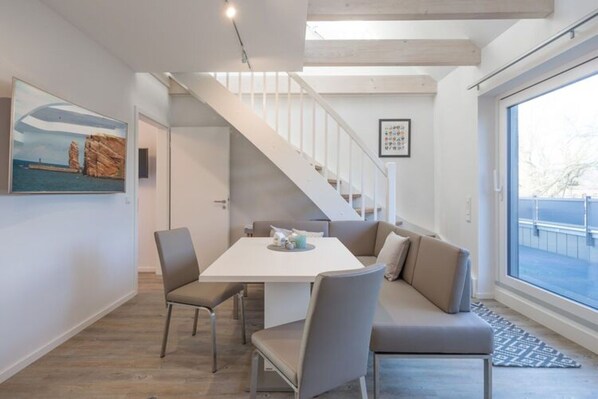 A modern interior with a dining area, a staircase, and a large window. - Ferienwohnung in Husum (Husum)
