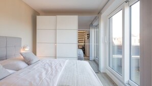 Ένα σύγχρονο υπνοδωμάτιο με ένα μεγάλο κρεβάτι, μια ντουλάπα και μια συρόμενη γυάλινη πόρτα που οδηγεί σε ένα μπαλκόνι.