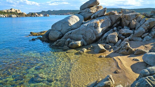 A rocky shoreline with clear water and distant hills.