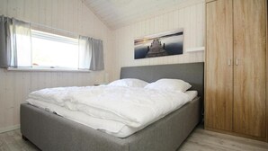A neatly made bed in a room with wooden walls and a window with curtains. - Ferienhaus Seebrise mit Sauna am Dummer See (Dümmer)