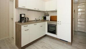 A compact kitchen with white cabinets, a built-in oven, a microwave, and a coffee maker. - Ferienhaus Seebrise mit Sauna am Dummer See (Dümmer)