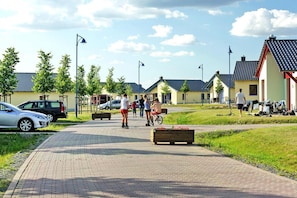A paved pathway with benches, parked cars, and houses with tiled roofs.