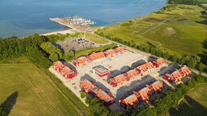 Vue aérienne d’une propriété située sur la côte, avec un port de plaisance, des bâtiments aux toits rouges et des champs verdoyants.