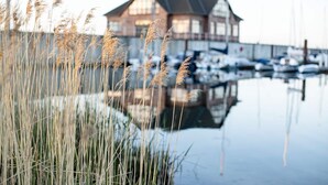Un port de plaisance avec des bateaux, un bâtiment doté d’un toit à pignon et de hautes herbes au premier plan.