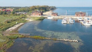 Un port de plaisance avec des bateaux amarrés, un petit bâtiment et une zone boisée en arrière-plan.